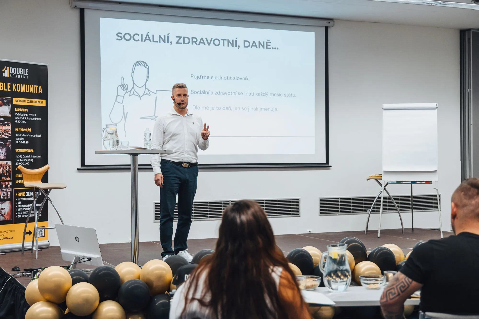 Lektor v bílé košili přednáší před projekcí o sociálním a zdravotním pojištění a daních.