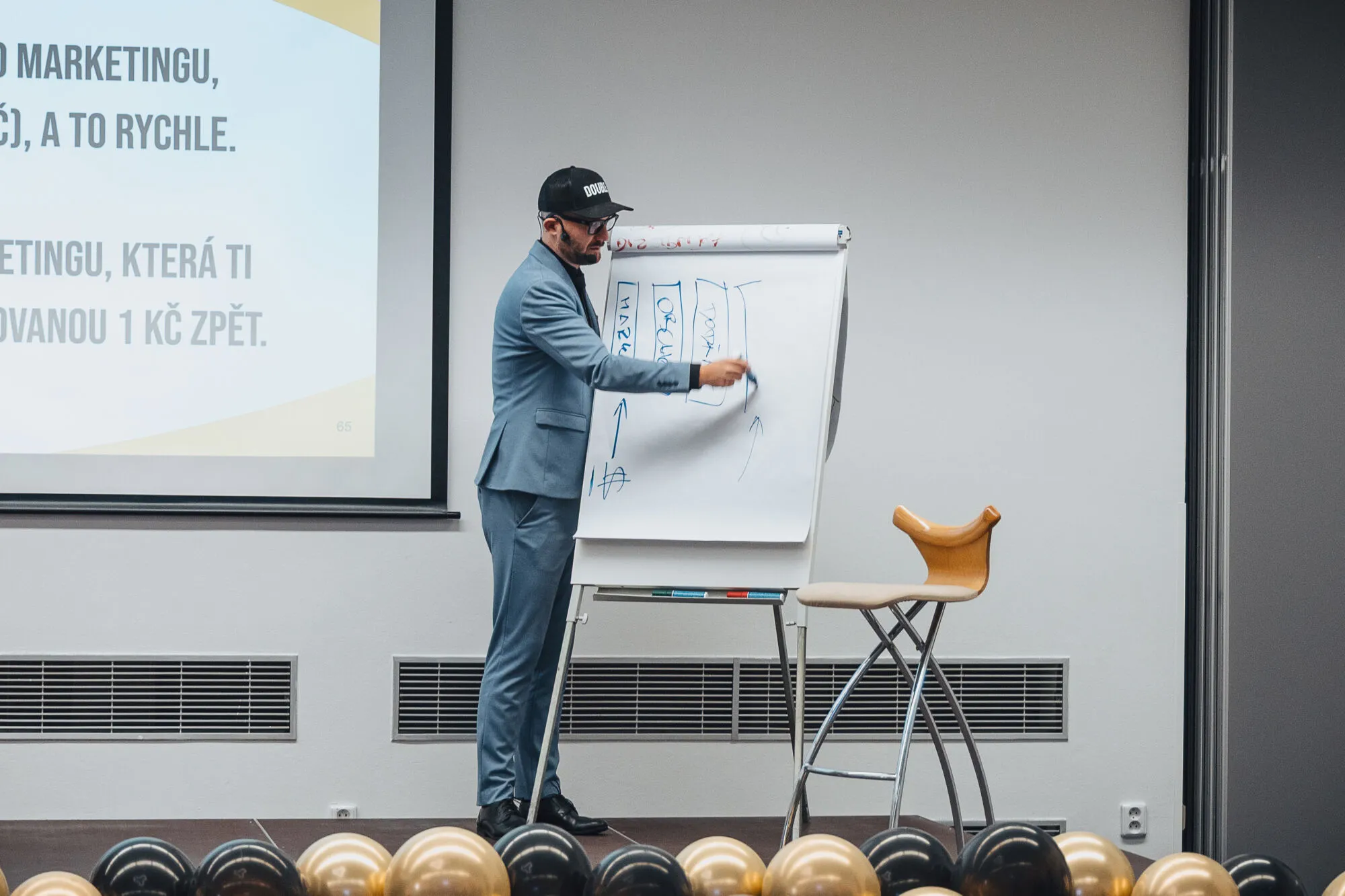 Lektor kreslí fixem schéma na flipchart vedle projekční plochy.