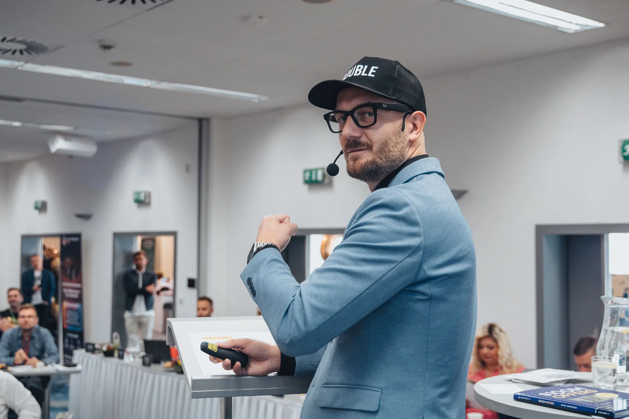 Lektor v modrém saku a černé čepici mluví k publiku na Boot Campu.