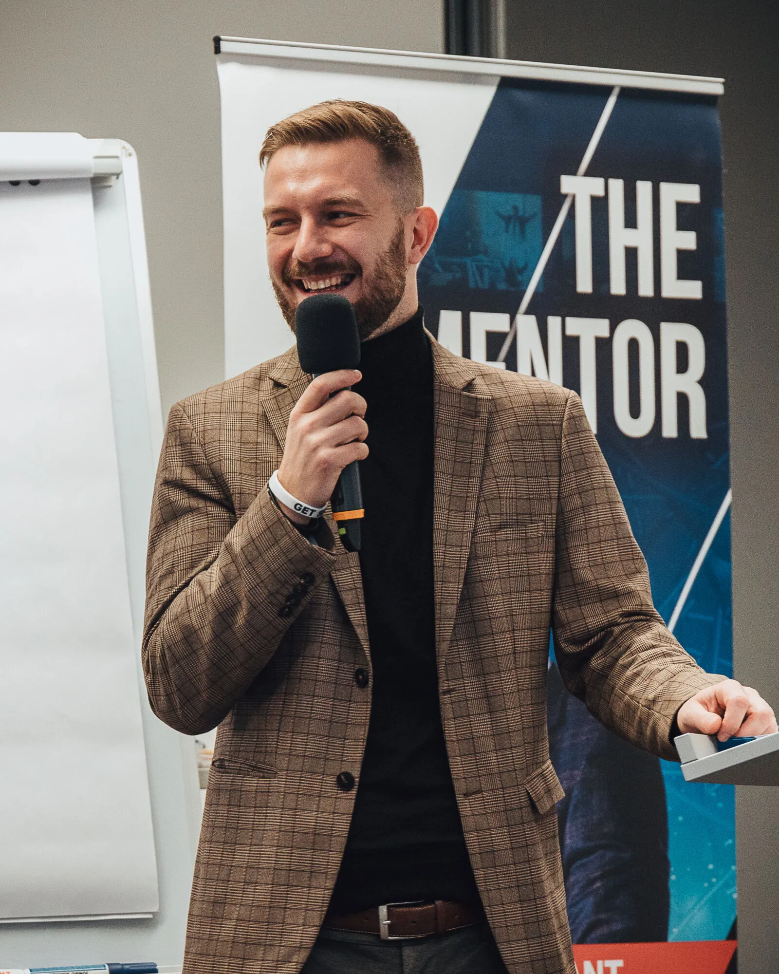 Usmívající se mentor v kostkovaném saku s mikrofonem v ruce.